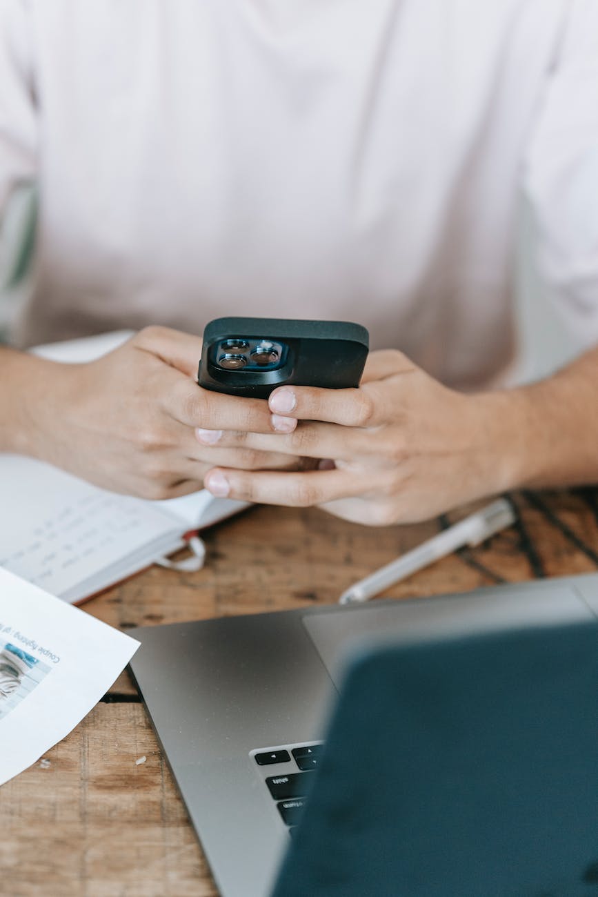 crop unrecognizable man using smartphone and working on laptop
