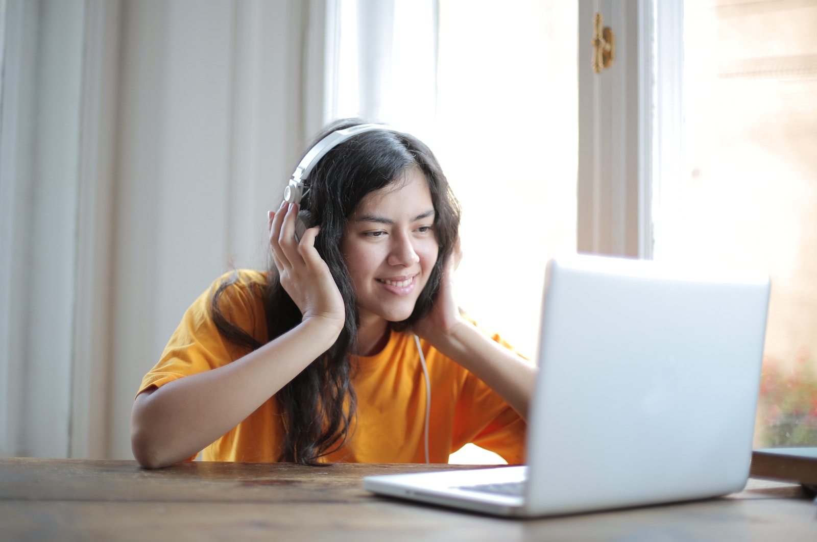 Woman in Orange Shirt Sitting by the Table Using Macbook